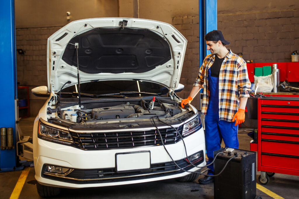 full length shot of handsome auto mechanic charging the battery using wire cables in modern service station